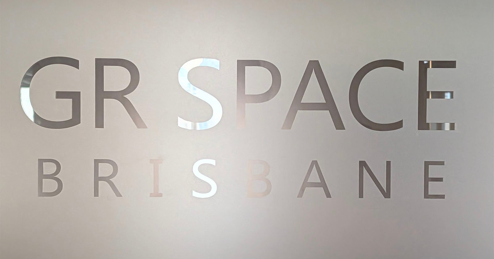Frosted glass with cut-out letters partially reading GR SPACE BRISBANE, with the background faintly visible through the transparent text. Frosted glass with cut-out letters partially reading GR SPACE BRISBANE, with the background faintly visible through the transparent text.
