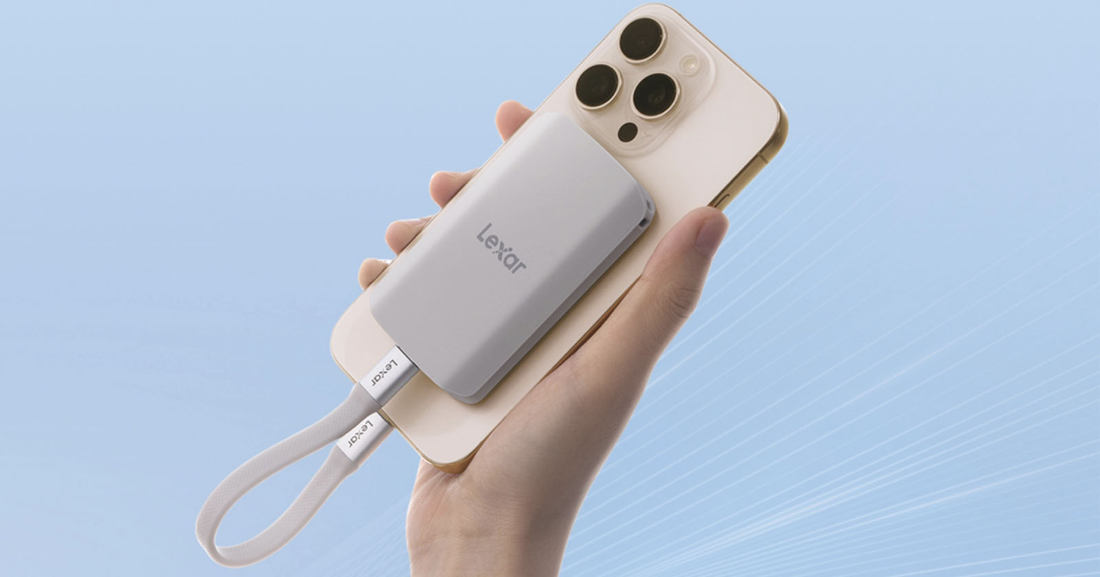 A hand holds a white smartphone with a silver Lexar external solid-state drive (SSD) attached to its back. A white strap labeled Lexar hangs from the SSD, and the background is a gradient light blue. A hand holds a white smartphone with a silver Lexar external solid-state drive (SSD) attached to its back. A white strap labeled Lexar hangs from the SSD, and the background is a gradient light blue.