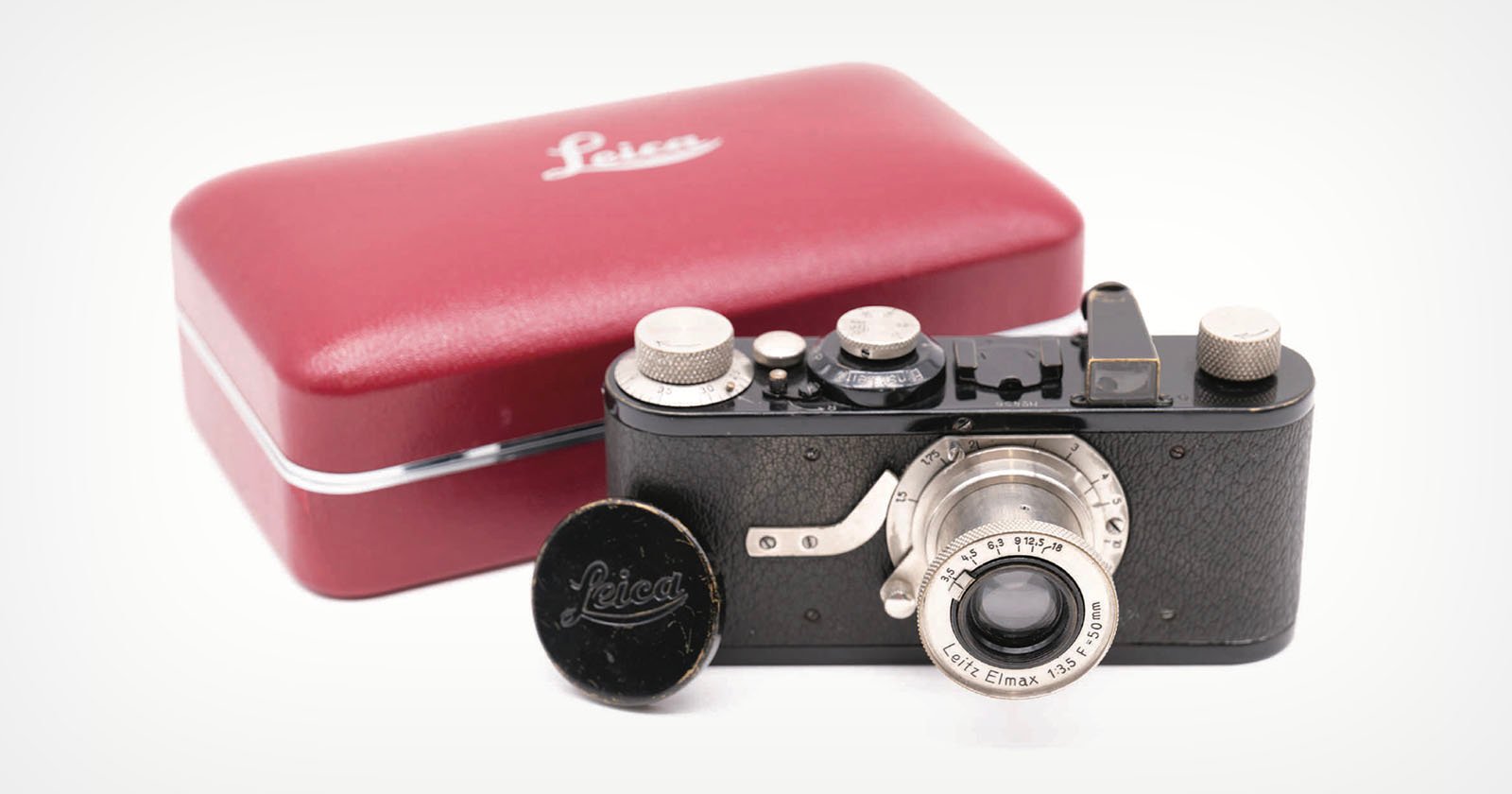 A vintage Leica camera with a lens cap beside it sits in front of a red Leica-branded case on a white surface. A vintage Leica camera with a lens cap beside it sits in front of a red Leica-branded case on a white surface.