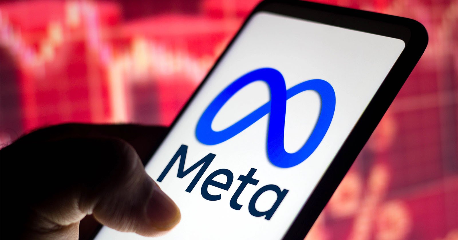 A hand holds a smartphone displaying the Meta logo and name, with a blurred red stock market graph in the background. A hand holds a smartphone displaying the Meta logo and name, with a blurred red stock market graph in the background.